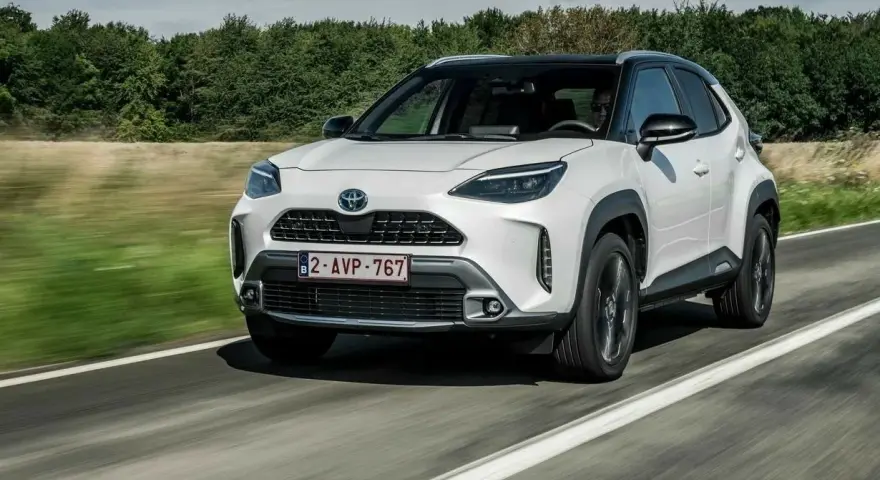 Biały Toyota Yaris Cross jedzie po drodze, otoczony zielenią.