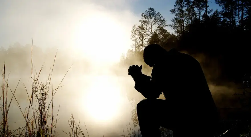 Silhouette eines Mannes, der im Morgennebel kniet und betet. Ein Bild, das christliche Glaubensbekenntnisse widerspiegelt.