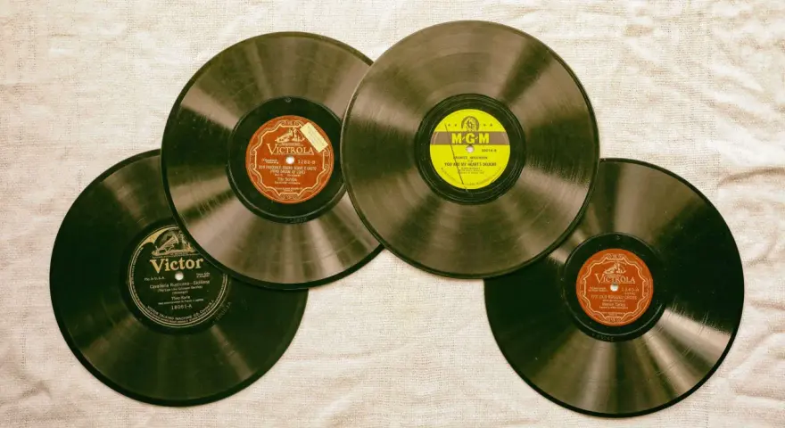 Vier alte Schallplatten liegen auf einer Leinwand. Eine davon hat ein gelbes MGM-Label, die anderen sind von Victrola und Victor. Sie erinnern an die Anfänge des Rocken Roll.