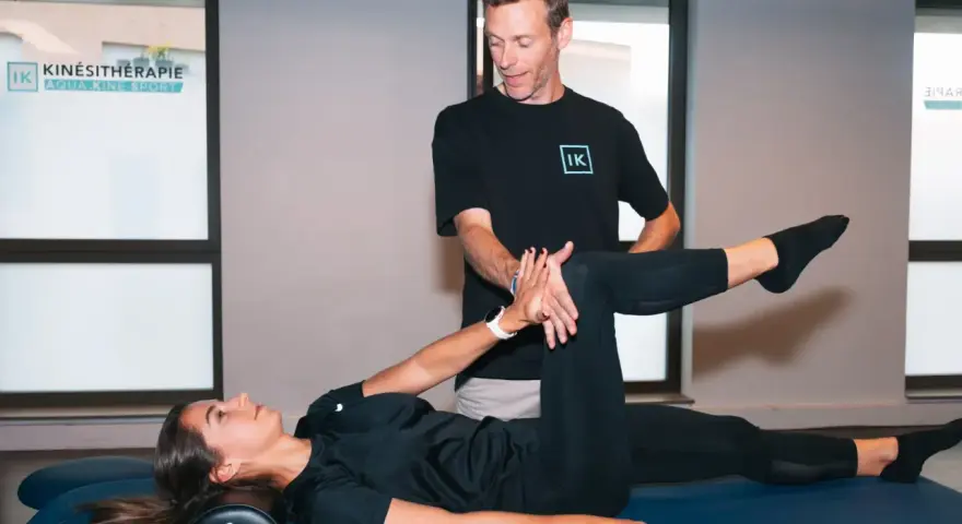 Un kinésithérapeute guide une patiente dans un exercice pour soulager la cruralgie. Elle est allongée sur une table de massage, une jambe pliée, l'autre tendue.