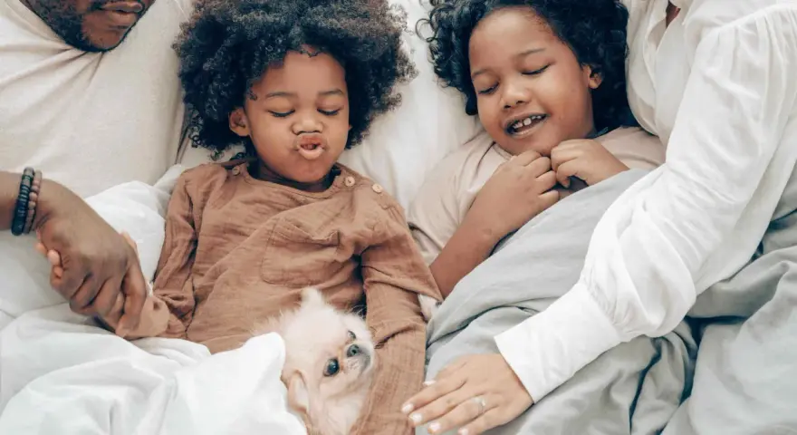 Familie kuschelt im Bett, um sich mit Kindern zu entspannen. Ein kleiner Hund liegt zwischen ihnen.