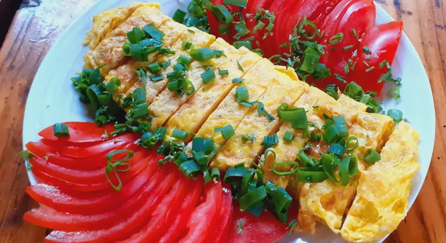 Pyszne koreańskie śniadanie: pokrojony omlet z jajek posypany szczypiorkiem, podany z plasterkami pomidora.