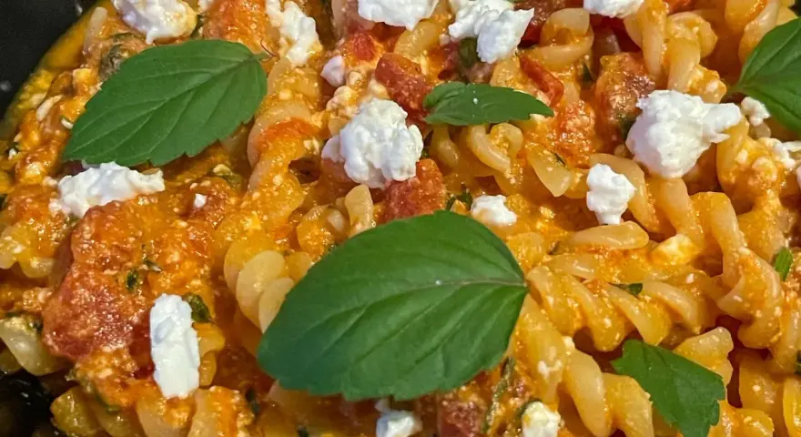 Makaron fusilli w pomarańczowym sosie z kawałkami sera i listkami bazylii.