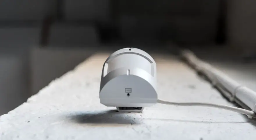 Detector de presencia y movimiento blanco, con cable, montado en superficie rugosa.