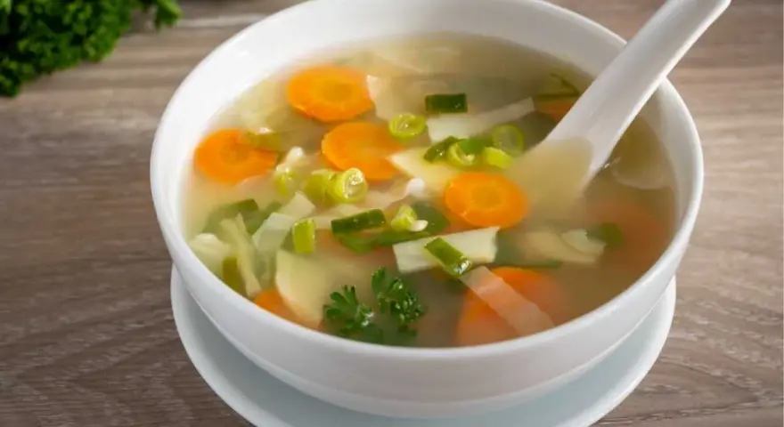 Tazón de sopa de verduras con zanahorias, puerros y perejil.