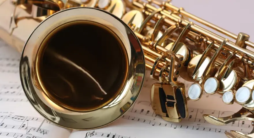 Ein glänzendes Musikinstrument, ein Saxophon, liegt auf Notenblättern. Seine goldene Oberfläche reflektiert das Licht.