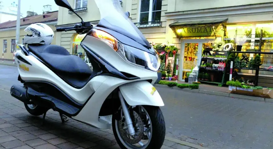 Biały skuter Piaggio X10 125, z kaskiem na siedzeniu, zaparkowany przed kwiaciarnią. Dane techniczne tego modelu są imponujące.