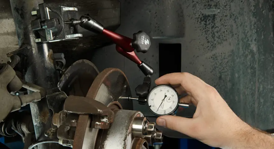 Mechanik mierzy bicie przy hamowaniu tarczy hamulcowej za pomocą czujnika zegarowego.