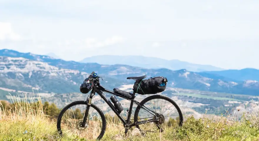 Rower gotowy do bike packingu, z sakwami na kierownicy i pod siodełkiem, na tle górskiego krajobrazu.