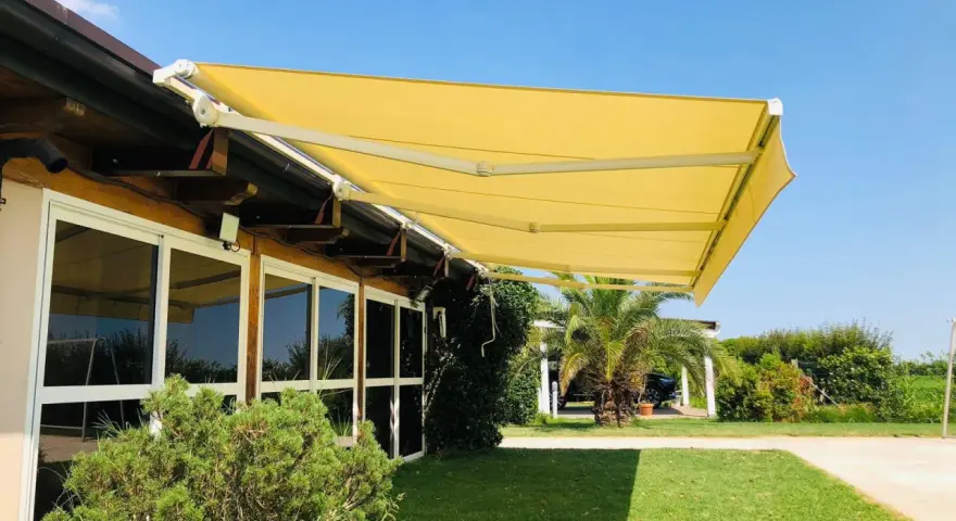 Tende da sole sconto in fattura, gialle e moderne, proteggono un edificio con ampie vetrate da un sole splendente.