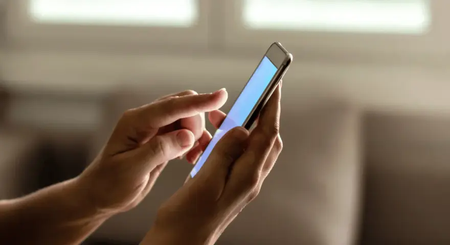 Dłonie trzymają smartfon, na ekranie którego wyświetla się niebieski kolor. Zastanawiasz się, jak sprawdzić ile lat ma telefon?