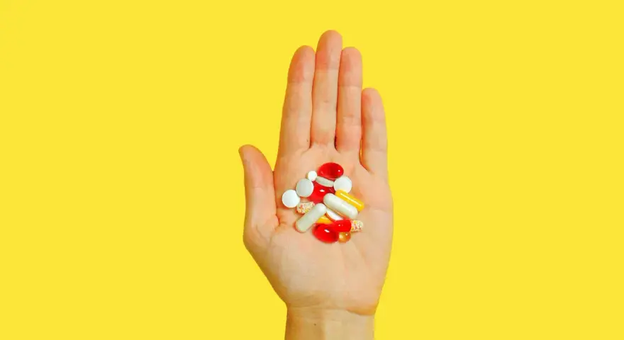 Hand hält bunte Pillen und Kapseln, die bei der Behandlung von Akne helfen könnten, wie z.B. Vitamin B5.