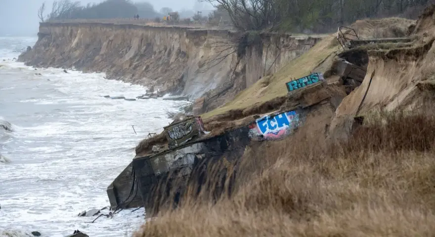 Ein alter Bunker am Strand, von der Erosion freigelegt und mit Graffiti bemalt, trotzt den Wellen.