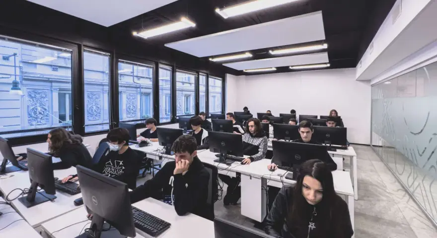 Giovani studenti concentrati davanti ai computer, un'aula moderna che ospita un corso di programmazione gratis.