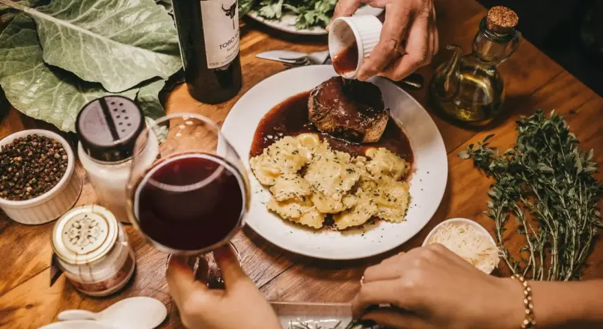 Elegancka kolacja z ravioli i wołowiną w sosie. Idealne pytanie: jakie wino do gotowania? Czerwone wino i świeże zioła dopełniają atmosferę.