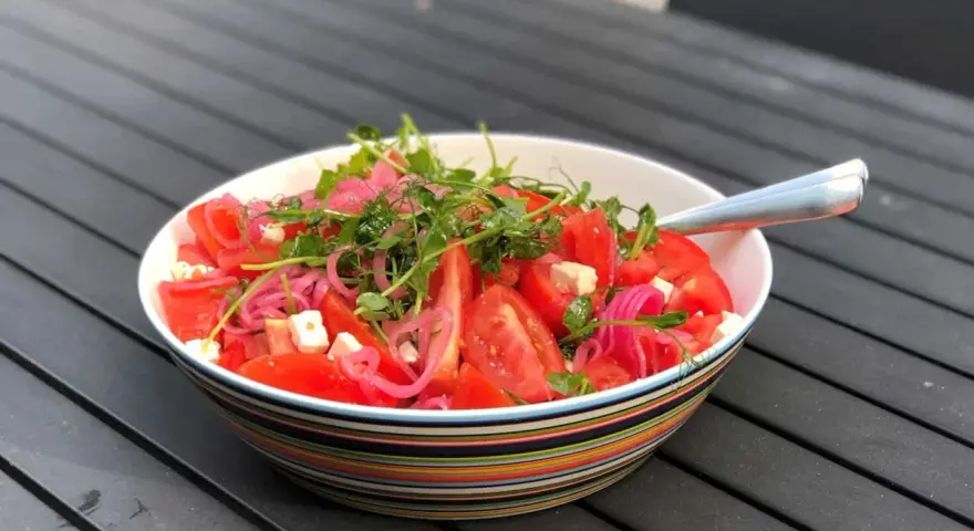 Enkel sallad med tomater, fetaost, rödlök och groddar i en färgglad skål.
