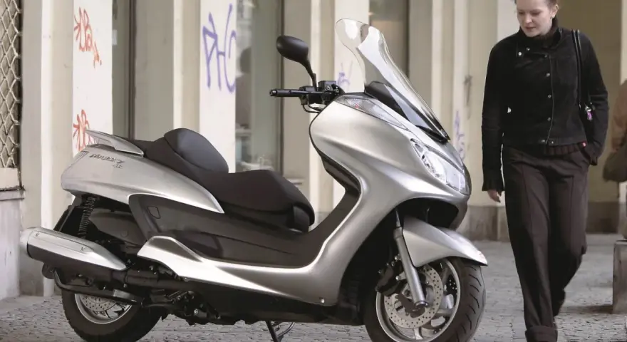Srebrny skuter Yamaha Majesty 400, symbol miejskiej elegancji, obok kobiety w ciemnej kurtce.