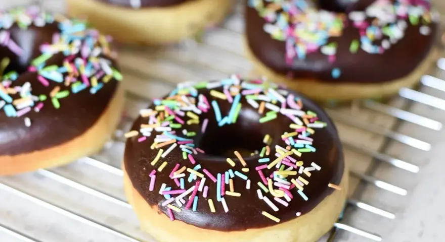 Färska, hembakade donuts med chokladglasyr och färgglatt strössel ligger på ett galler. Perfekt för att baka donuts!