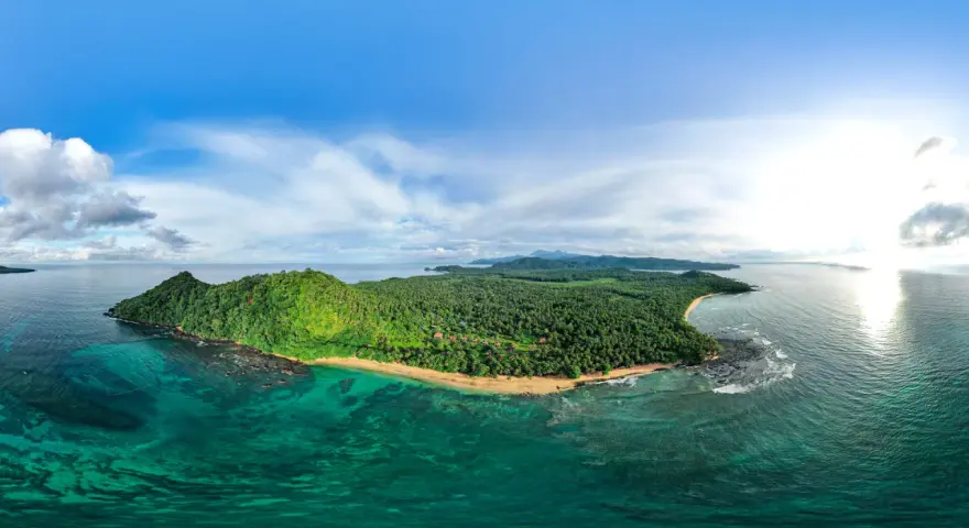 Zielona wyspa z palmami i plażą, otoczona turkusową wodą. Widok na Sao Tome z lotu ptaka.