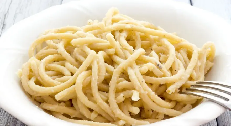 Pici, pasta fatta a mano con un'origine antica, servita in una ciotola bianca con una forchetta.