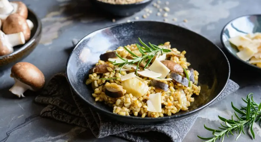 Miseczka risotto z grzybami i parmezanem, udekorowana rozmarynem.