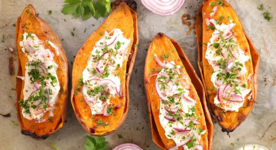 Quatre moitiés de patate douce au four, garnies de crème, oignons rouges et persil. Un délice simple et savoureux.