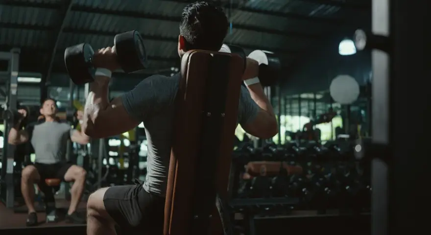 Två män tränar axlar med hantlar på ett gym. En fokuserar på push, den andra på pull.