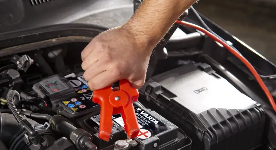 Starthilfe: Rote Klemme am Pluspol, warum nicht minus an minus? Ein Mann klemmt ein Starthilfekabel an die Autobatterie.