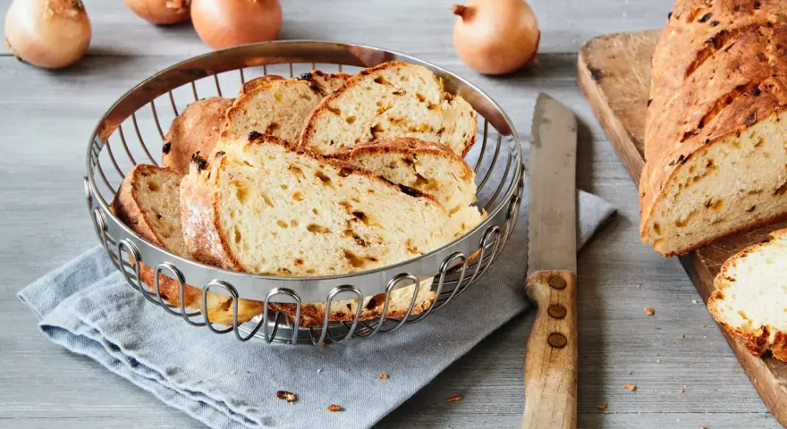Frisch gebackenes Zwiebelbrot, bereit für ein leckeres Zwiebelbrot Rezept. Ganze Zwiebeln liegen daneben.