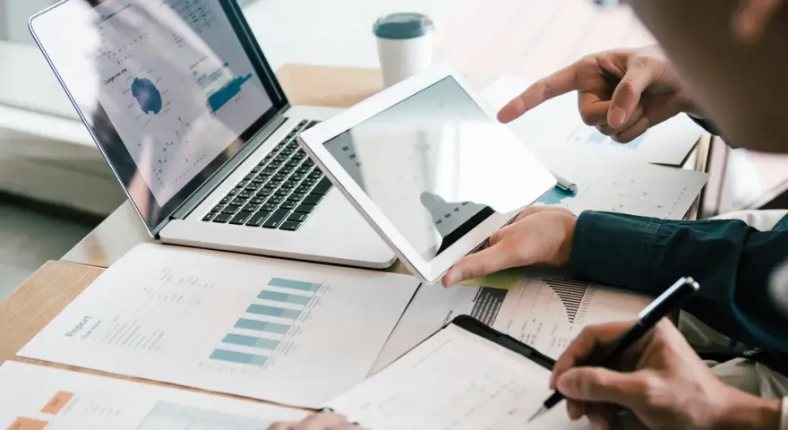 Analyse de rapports financiers sur tablette et ordinateur portable, illustrant la gestion administrative d'une entreprise.