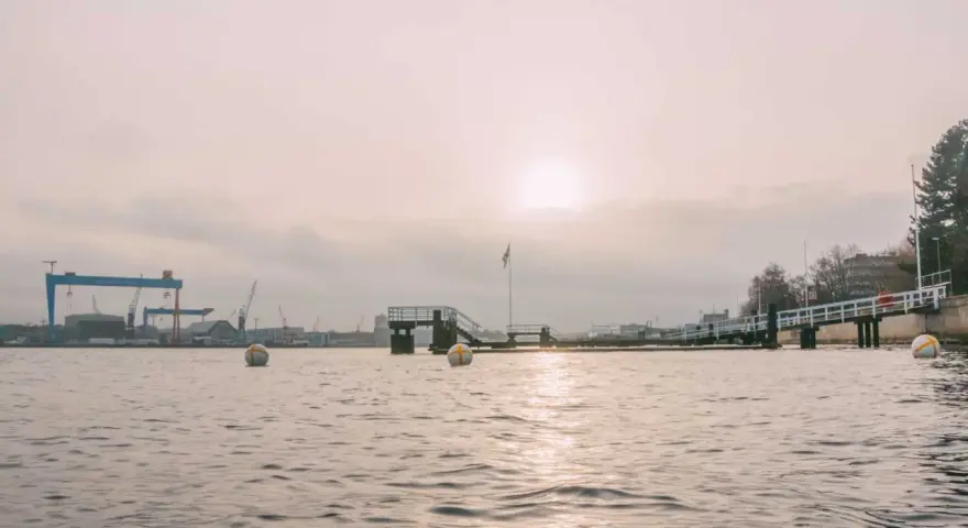 Kiel im Winter: Hafenkräne und eine Mole im nebligen Licht. Bojen treiben auf dem ruhigen Wasser.