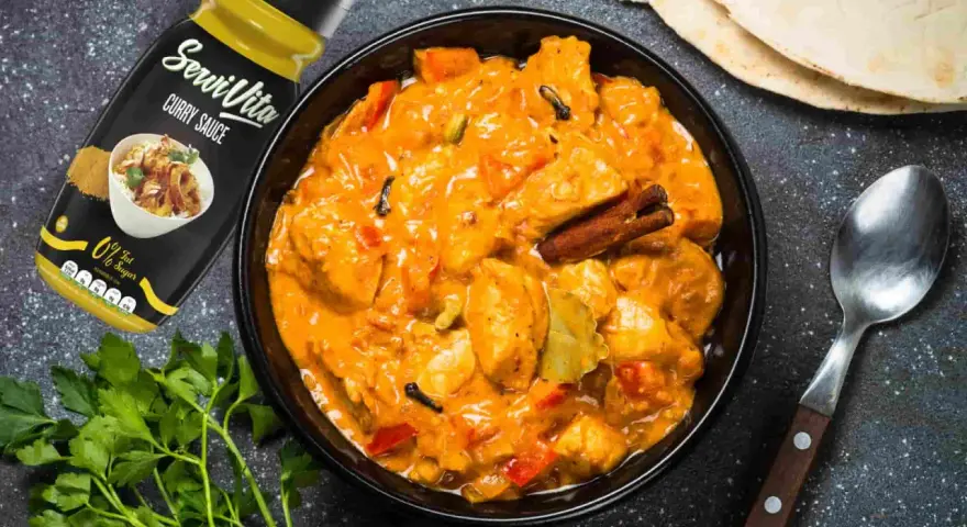 Bol de pollo al curry cremoso con especias, salsa y pan naan al lado.