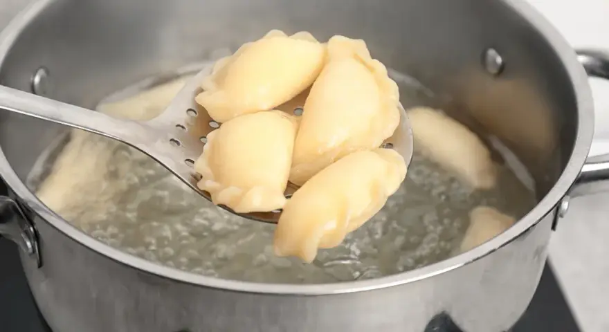 Pierogi gotujące się w garnku, wyjmowane łyżką cedzakową.