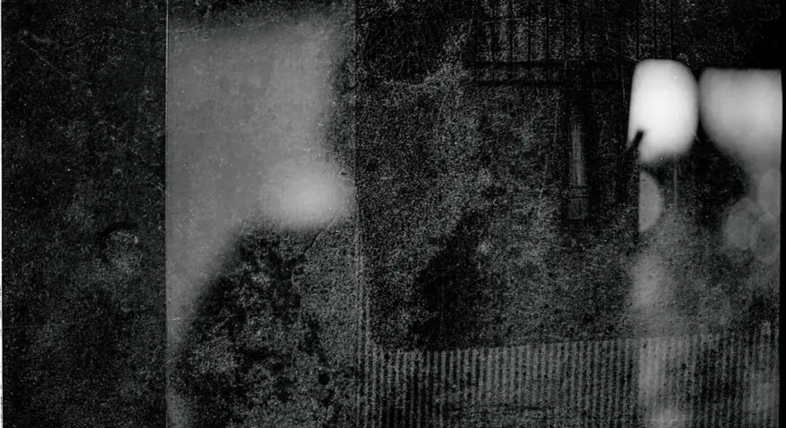 Mroczna, ziarnista fotografia. Widać fragmenty twarzy, być może portret autorstwa Mariusza Gajewskiego, z rozmytymi światłami i teksturami.