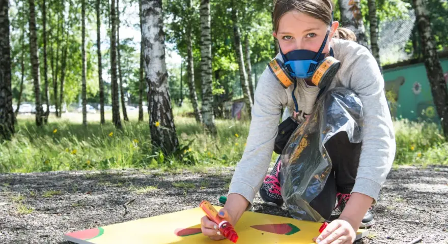 Ung flicka med munskydd skapar graffiti på papper utomhus.