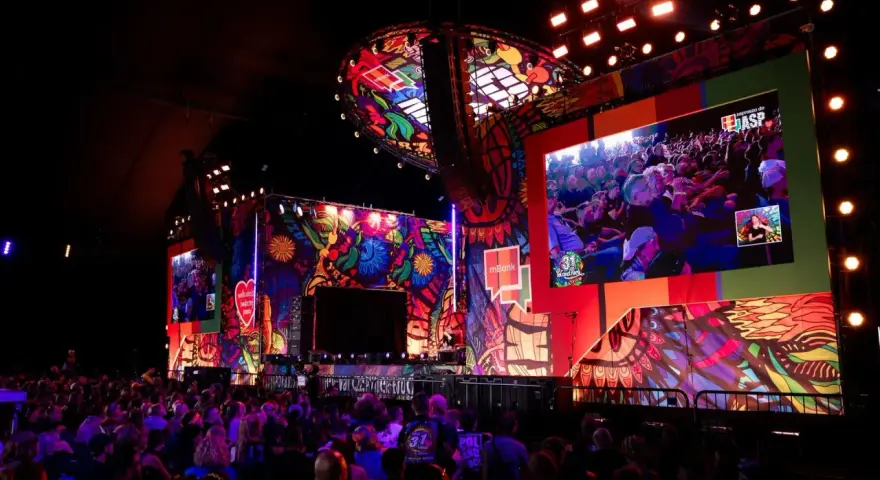 Kolorowa scena festiwalu Poland Rock 2026 z wielkim ekranem pokazującym publiczność. Tłum widzów wpatrzony w widowisko.