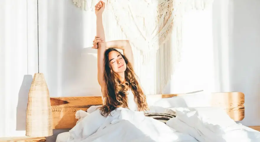 Eine Frau streckt sich im Bett aus, umgeben von weißer Bettwäsche. Sie genießt den Morgen, bereit, zusammen einzuschlafen und den Tag zu beginnen.