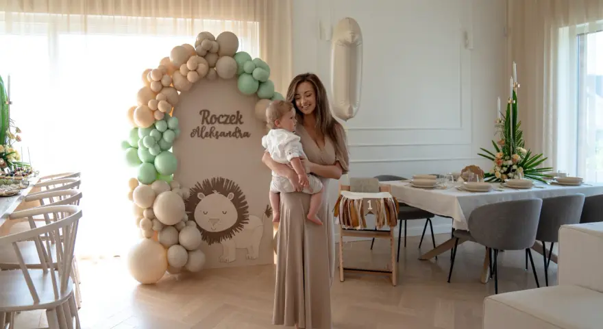 Elegancka sukienka i sandałki to świetny wybór, jak się ubrać na roczek jako gość. Uroczystość w stylu safari z lwem i balonami.