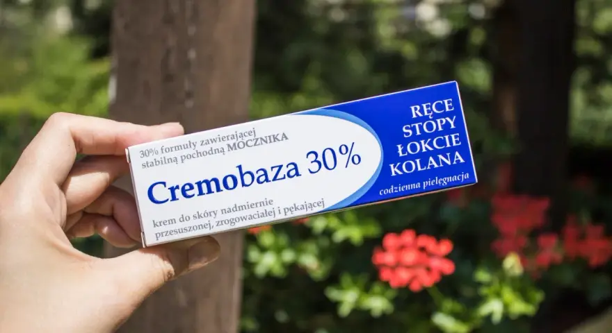 Dłoń trzyma opakowanie kremu Cremobaza 30%, przeznaczonego do pielęgnacji suchej, zrogowaciałej skóry dłoni, stóp, łokci i kolan.