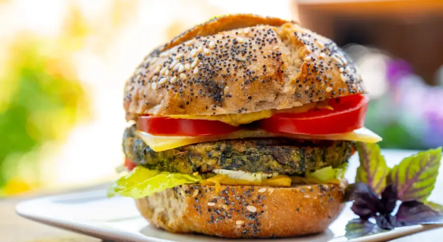 Deliciosa hamburguesa de espinacas con pan de semillas, queso, tomate y lechuga, servida en un plato blanco.