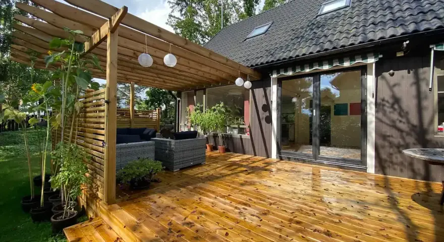 Trall med synliga skruvar kan vara en nackdel för utseendet. Här en altan med pergola, utemöbler och solrosor.