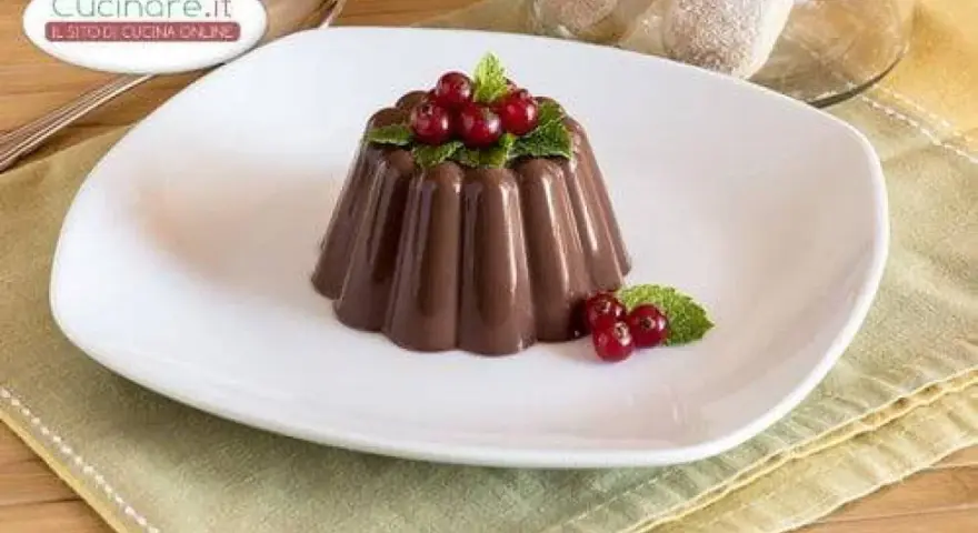 Budino al cioccolato decorato con ribes rossi e menta, servito su un piatto bianco.