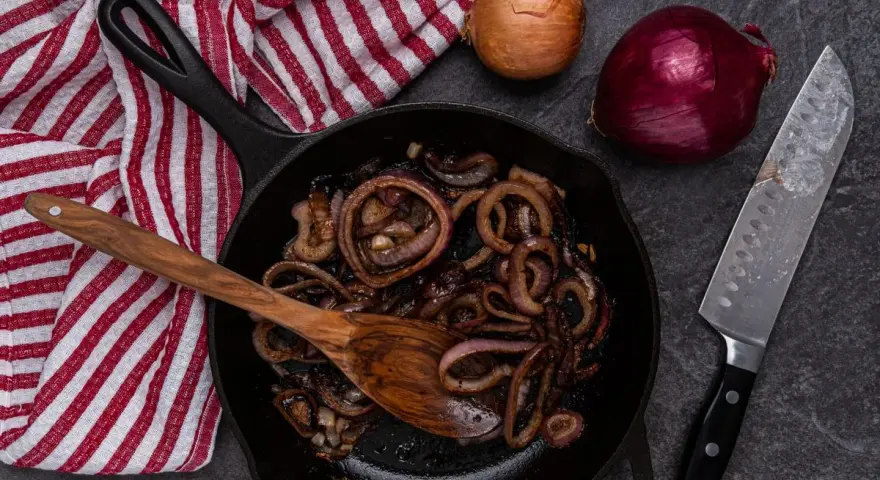 Cipolle in agrodolce caramellate in padella, pronte per essere gustate. Accanto, cipolle fresche e un coltello affilato.