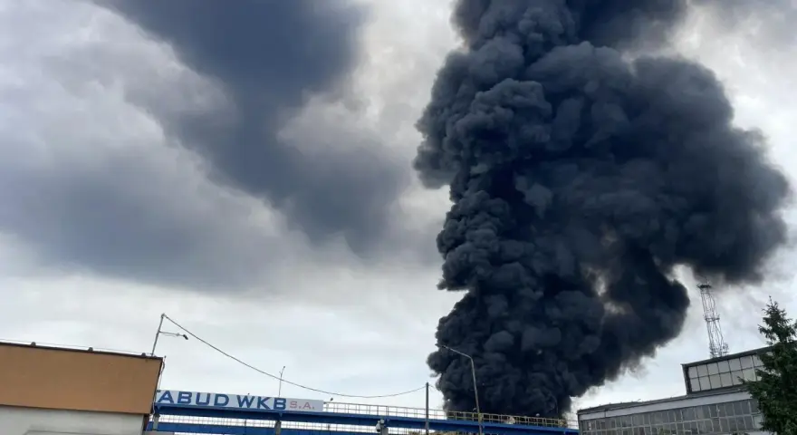 Ogromny słup czarnego dymu unosi się nad budynkami, świadcząc o pożarze wysypiska.
