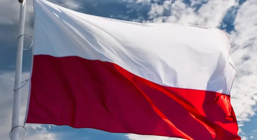 Flaga biało-czerwona powiewa na wietrze na tle błękitnego nieba z chmurami.