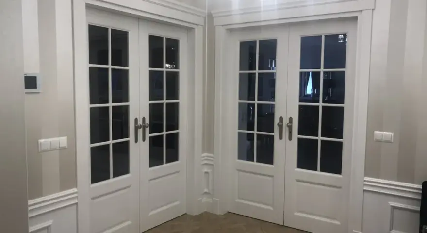 Eleganckie białe drzwi dwuskrzydłowe z przeszkleniem, osadzone w metalowych futrynach, tworzą stylowe przejście.