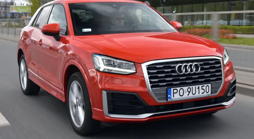Czerwone Audi Q2 w ruchu miejskim. Choć jego design jest atrakcyjny, warto rozważyć potencjalne wady, takie jak ograniczona przestrzeń bagażowa.