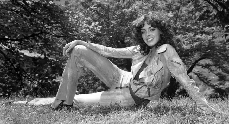 Nadia Cassini, con il suo fisico prorompente, posa su un prato, sfoggiando un completo giacca e pantaloni.
