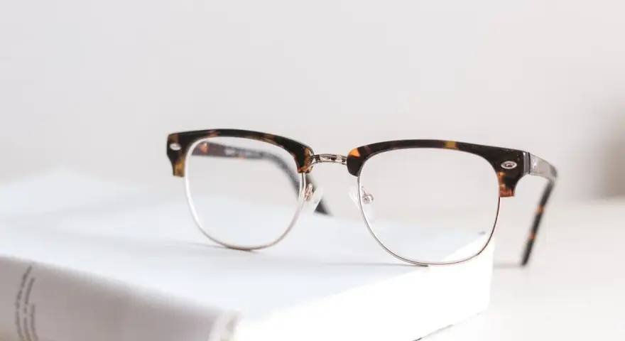 Okulary z oprawkami w stylu clubmaster leżą na białej książce. Czy wada 0.75 to powód, by nosić okulary?