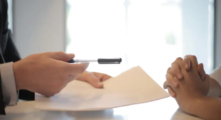 Man en traje entrega documento a persona con manos entrelazadas, discutiendo cómo devolver fianza alquiler antes finalizar contrato.